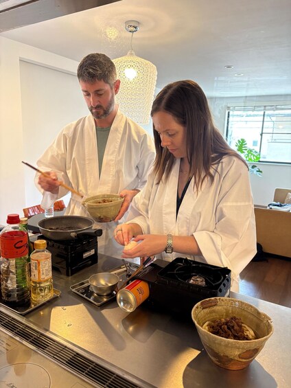Two people cooking in a modern kitchen with a decorative light fixture above the stove. 2