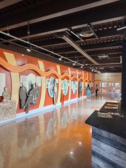 An indoor exhibition with a wall of historical figures and information panels. 5