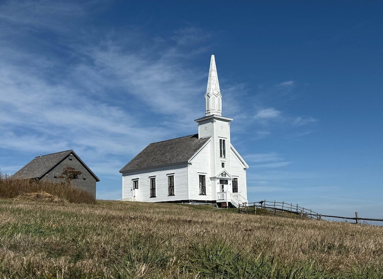 A white church with a steeple on a grassy hill under a clear sky. 1
