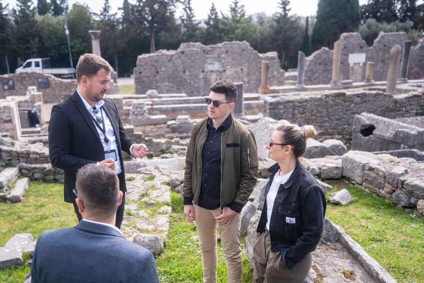 A group of people standing in an ancient ruin with stone columns and walls. 3