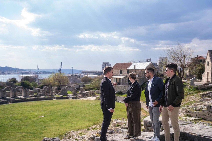 A group of people standing on a grassy area with ancient ruins in the background. 2