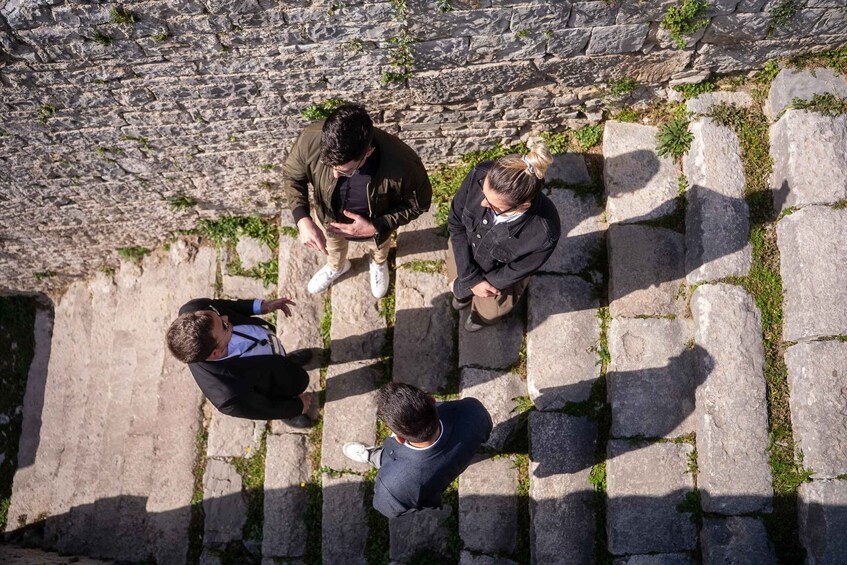 Three people standing on a stone-paved path with a stone wall in the background. 4