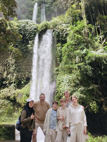A family posing in front of a waterfall surrounded by lush greenery. 3
