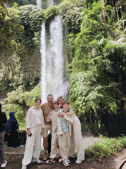 A family posing in front of a waterfall surrounded by lush greenery. 5