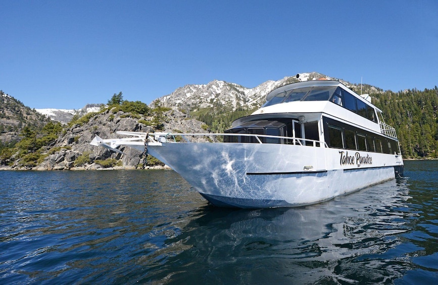 A white boat named Tahoe Paradise on a calm lake with rocky mountains in the background. 2