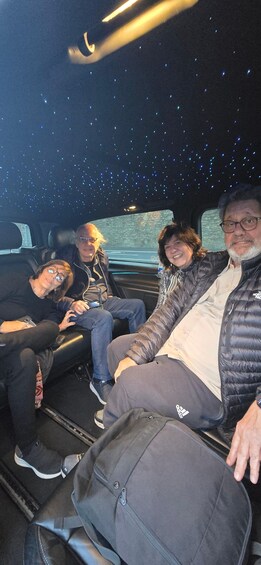 Four people seated in a vehicle with a starry ceiling. 4