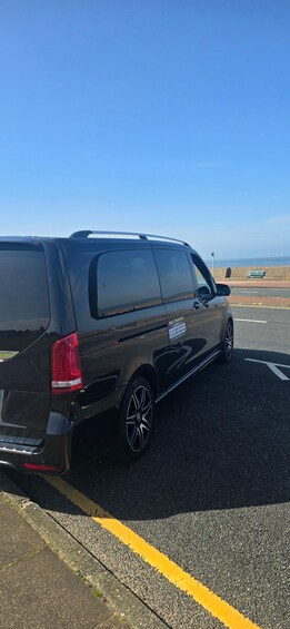 A black van parked on a road with a clear blue sky and a distant view of wind turbines. 3