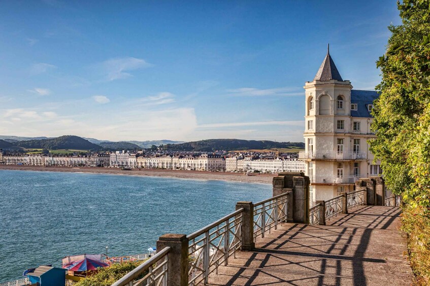 A coastal town with a prominent tower, a promenade, and a view of the sea and distant hills. 2