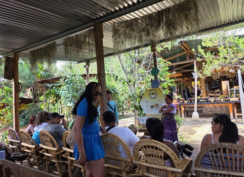 A covered outdoor seating area with wicker chairs, surrounded by lush greenery and a rustic wooden structure. 2