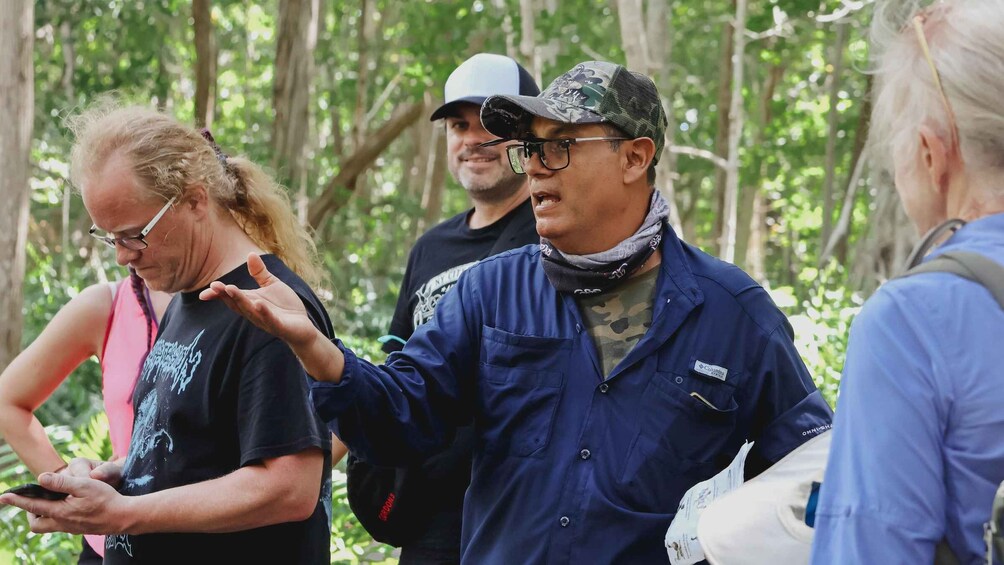 A group of people in a forested area, some wearing hats and one person gesturing while holding a smartphone. 2