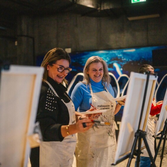 Two people painting on easels in an indoor setting. 5
