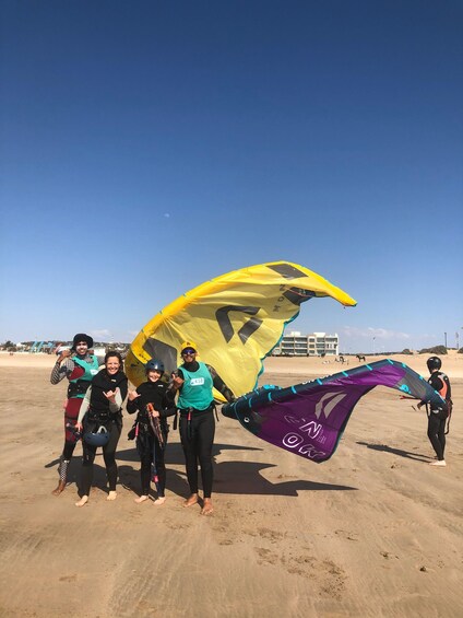 A group of people on a sandy beach with a large yellow and purple kite. 2