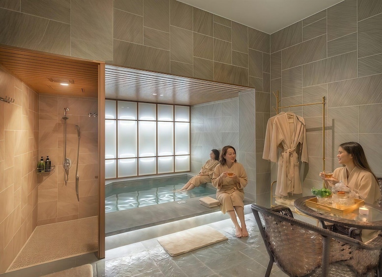 A modern spa with a glass-enclosed hot tub, wooden paneling, and a seating area with a table. 1