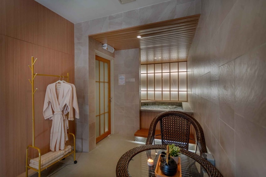 A spa room with a wooden wall, a glass table with a candle, and a chair. 2