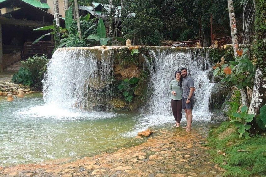 A waterfall, a person standing on a stone path, and lush greenery. 1