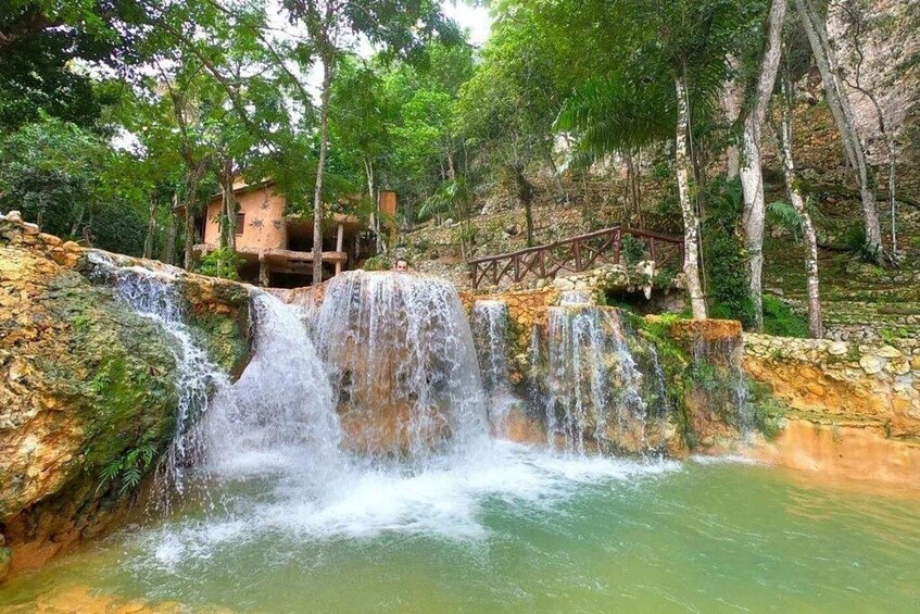 A waterfall cascading over rocks into a pool, surrounded by trees and a wooden bridge. 2