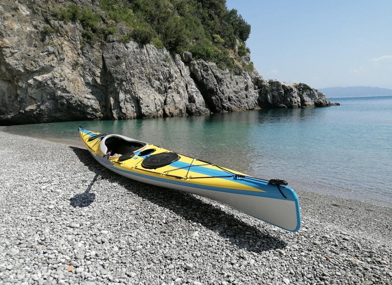 A yellow and blue kayak on a pebble beach with a rocky cliff in the background. 3