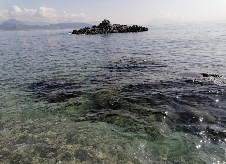 A rocky island in clear water with mountains in the background. 2
