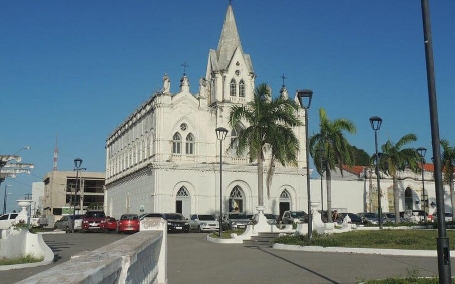 A white church with a pointed steeple, palm trees, and parked cars. 3