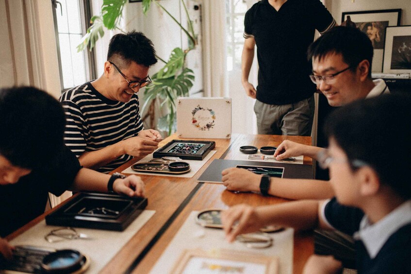 A group of people engaged in a board game at a wooden table with a laptop and various game pieces. 3
