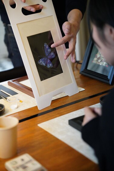 A person holding a framed butterfly photograph. 5