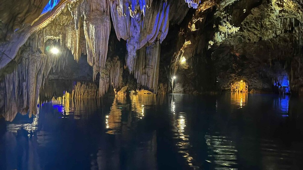 A cave with stalactites and stalagmites, illuminated by artificial lights, and a calm pool of water reflecting the formations. 5