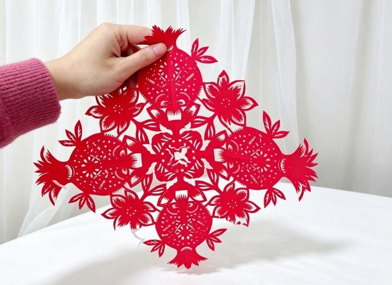 A hand holding a red paper cut-out with a floral pattern. 2