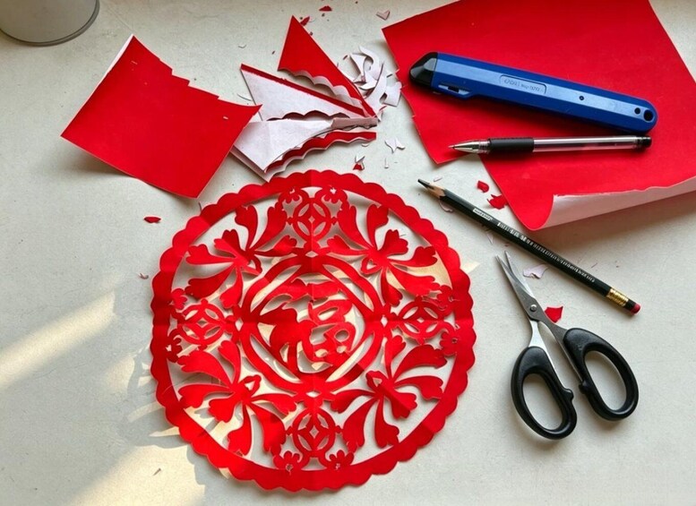 A red paper cut-out, scissors, a blue pen, and a pencil on a table. 4