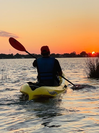 A person kayaking on a body of water during sunset. 1