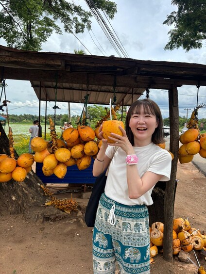 A person holding a coconut under a wooden structure with more coconuts hanging above. 2