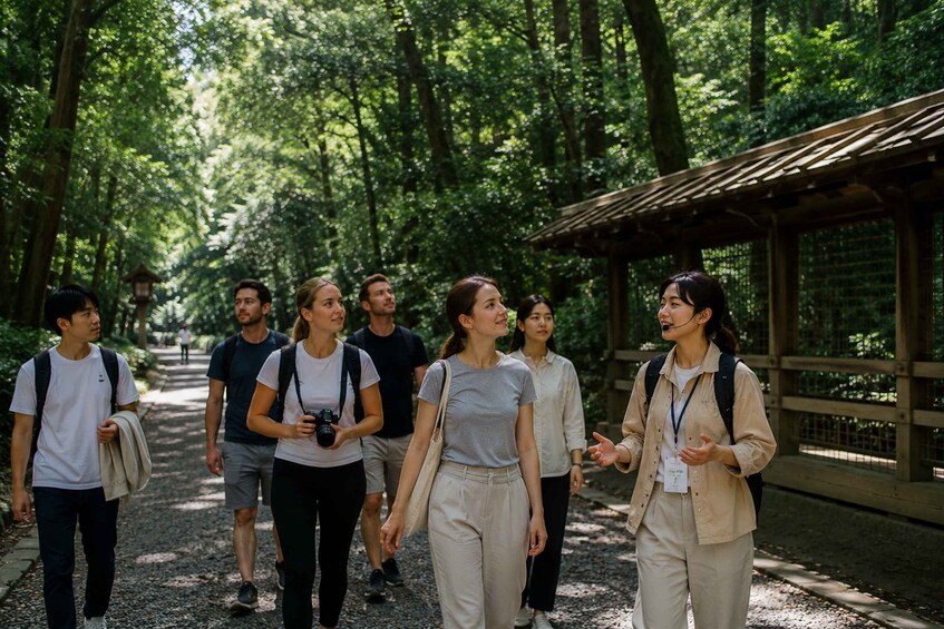 A group of people walking on a forested path with a wooden structure on the right. 1