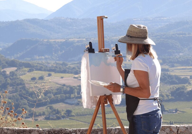 A person painting a landscape with a view of rolling hills and mountains in the background. 2