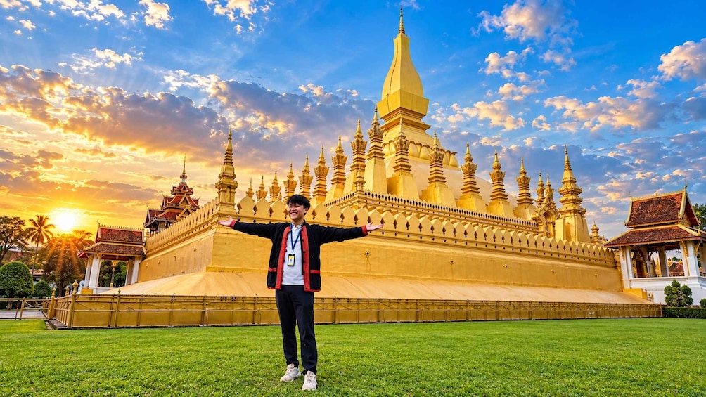 A person standing in front of a large golden temple with multiple spires, set against a sunset sky. 2