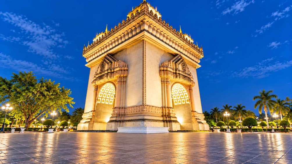 A well-lit monument with intricate carvings and a symmetrical design, surrounded by a paved plaza and palm trees. 5