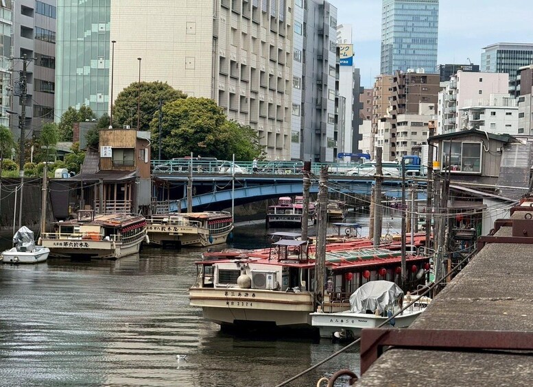 A river with boats docked, a bridge, and modern buildings in the background. 1