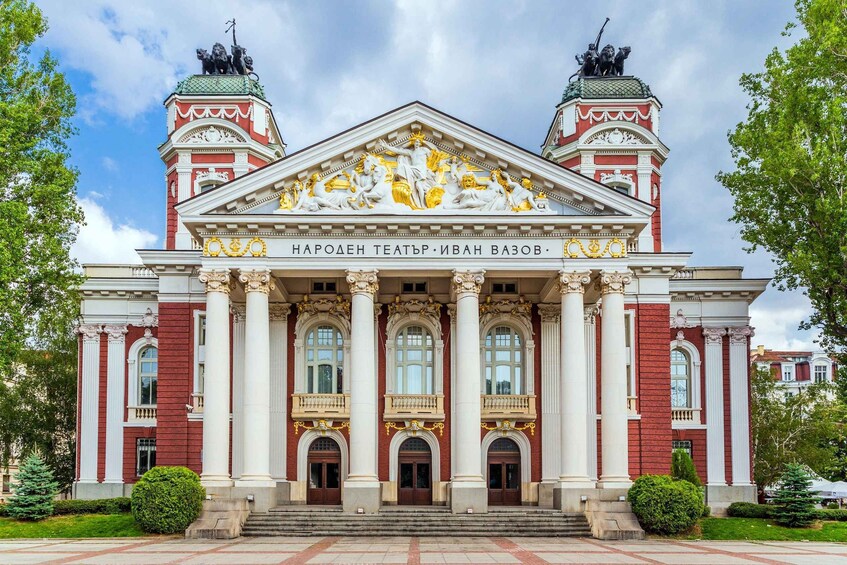 A grand building with red and white architecture, featuring columns and statues on the roof. 3