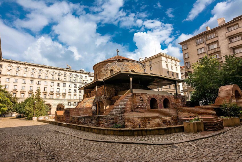 A historic brick structure with a dome and cross, surrounded by cobblestone streets and modern buildings. 4