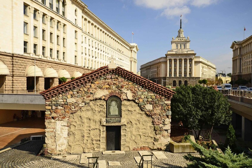 A historic stone building with a tiled roof, a plaque, and a statue in front. 2