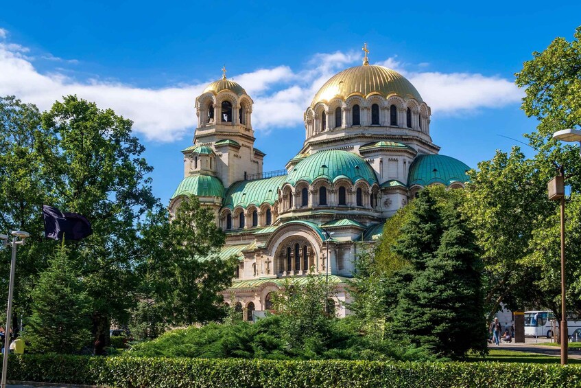 A large cathedral with multiple domes and a bell tower, surrounded by lush greenery and trees. 1