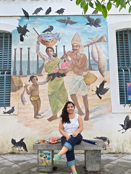 A mural of fishermen and a woman on a bench in front of it. 1