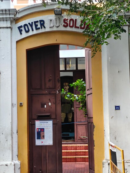 A building entrance with a sign reading 'FOYER DU SOLDO' and a mannequin in a uniform. 4