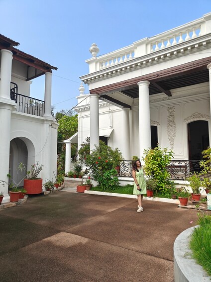 A woman standing in a courtyard with a white building featuring columns and a balcony. 5