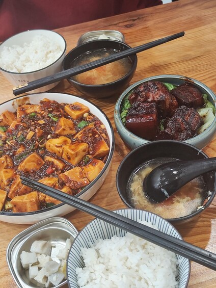 A variety of dishes including tofu, meat, and rice, served on a wooden table. 3