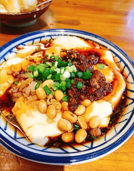 A bowl of tofu topped with green onions, peanuts, and a dark sauce. 2
