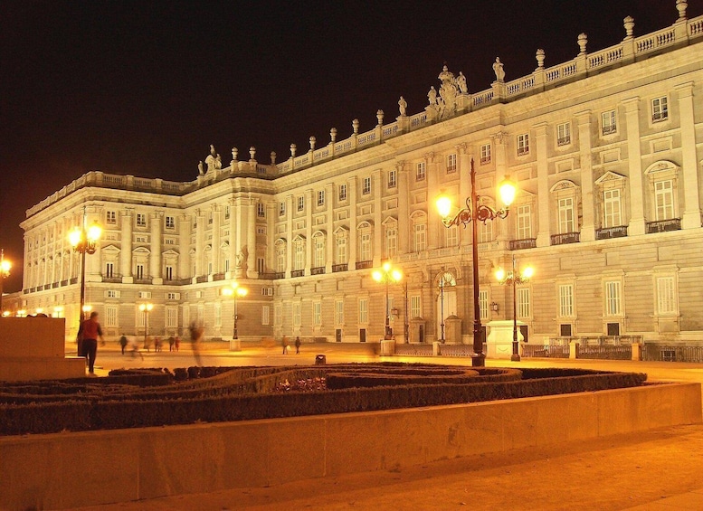 A grand illuminated building with classical architecture, surrounded by a formal garden and street lamps. 5