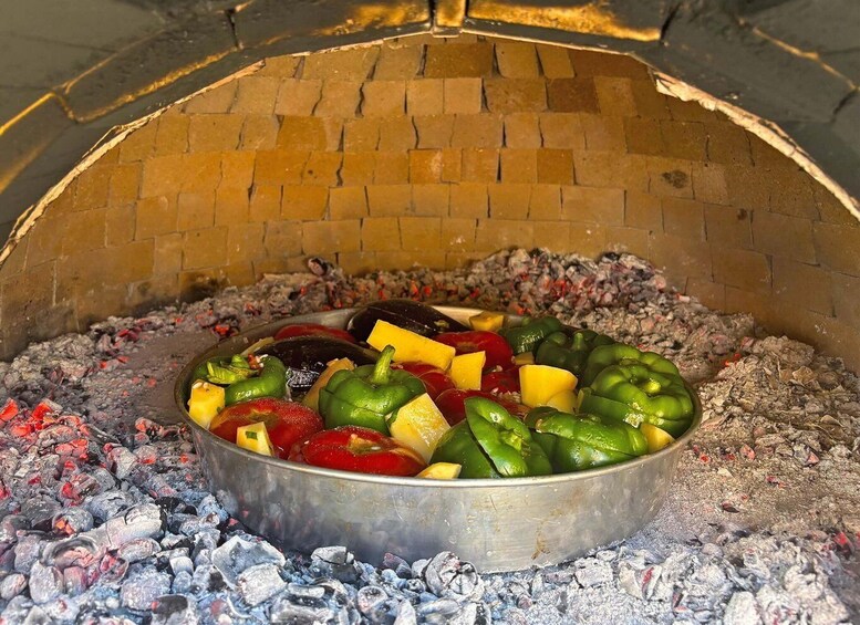 A metal pot filled with vegetables cooking over charcoal in a brick oven. 2