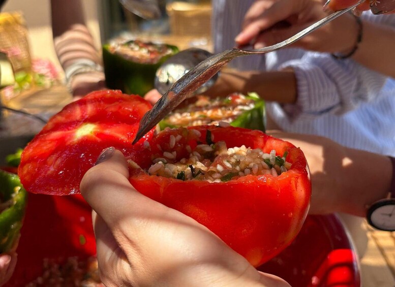 A person holding a halved red bell pepper with a spoon inside, filled with a mixture of grains and herbs. 5