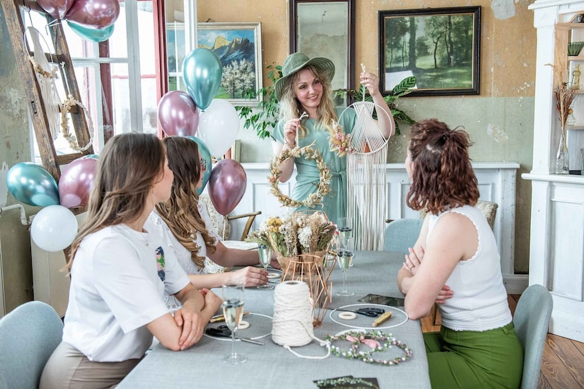 A group of people at a table with balloons, a wreath, and a white chair. 1