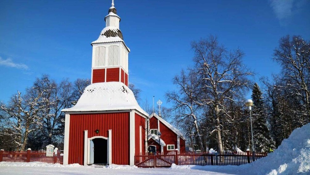 A red church with a white steeple, surrounded by snow-covered trees and a clear blue sky. 2