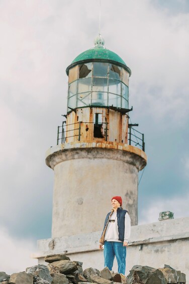 A person standing in front of a lighthouse with a green top and rusted base. 1